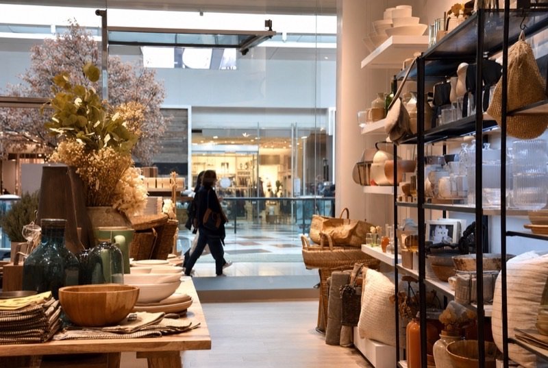 Indoor mall shop with tidy shelves of ceramics and home goods while a shopper walks past outside